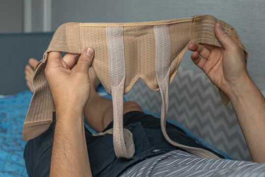 A man lies in bed and holds a medical bandage after surgery to remove an inguinal hernia.