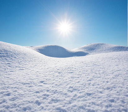 Beautiful winter landscape with bright sunburst shining down on smooth white snow hills under a clear blue sky.
