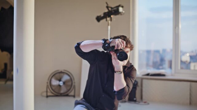 Photographer shooting model studio session. Man kneeling with camera by window.