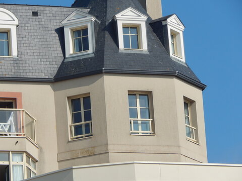 Maison de style baln&eacute;aire avec toiture en ardoise observ&eacute;e depuis la plage de Saint-Malo, architecture typique de la c&ocirc;te bretonne sous un ciel bleu ensoleill&eacute;.