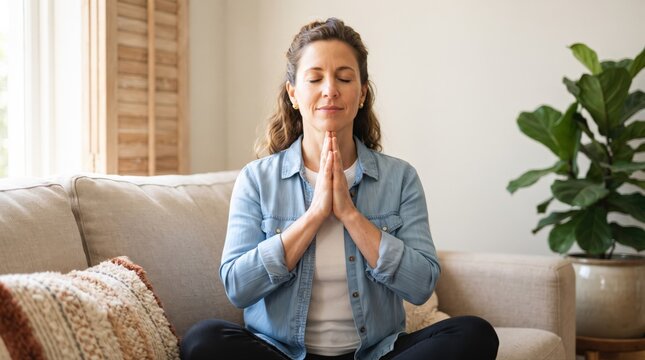 A tranquil woman practices meditation on a sofa, finding inner peace and promoting mental wellness. This serene home activity supports a balanced and mindful lifestyle.