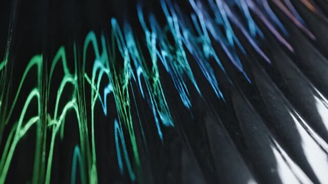 Close-up of iridescent wavy patterns on a dark surface, showing a gradient of green, blue, and purple light reflections.
