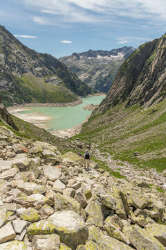 Guttannen, Switzerland. Hikers descending rocky alpine trail toward Gelmersee surrounded by granite peaks in the Bernese Alps
