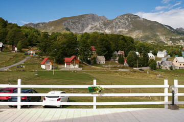 Fototapeta premium Scenic view of a mountain village with small houses, green slopes and rocky peaks in Durmitor, Montenegro