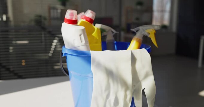 Cleaning bucket and gloves with sprays closeup. Blue pail of bottles, supplies and tools in a modern office, implying janitorial service and upkeep. Neat office hygiene concept for businesses.