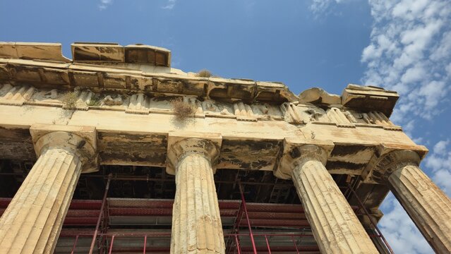 Athens, Greece - 8 July 2026. Low Angle View of the Temple of Hephaestus highlighting Doric columns, the carved frieze, weathered stonework and restoration scaffolding beneath a blue sky.