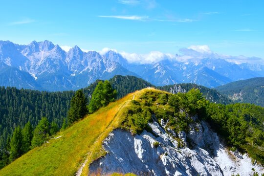 Hiking trail at a mountain ridge at Trupijevo Poldne woth a green meadow at one side and a rock precipice on the other and a view of the Julian alps in Gorenjska, Slovenia