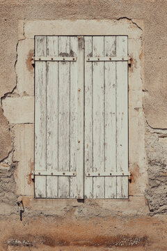 Aged wooden shutters on a weathered stucco wall in Burgundy, France, highlighting rustic architecture, texture, and traditional French village design.