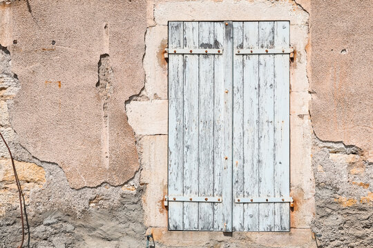 Aged wooden shutters set into a weathered stone and stucco wall in Burgundy, France, highlighting rustic architecture, texture, and rural French character.