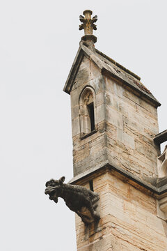 Historic church tower in Beaune, Burgundy, France, featuring a prominent stone gargoyle and Gothic architectural details against a bright sky.