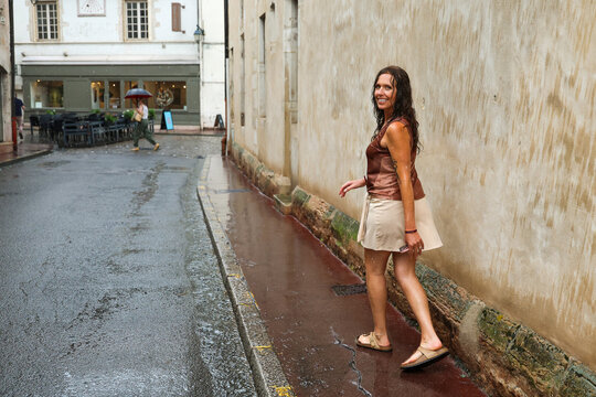 Woman walking along a rain-soaked street in Beaune, Burgundy, France, after a summer shower, surrounded by historic architecture and old stone buildings.