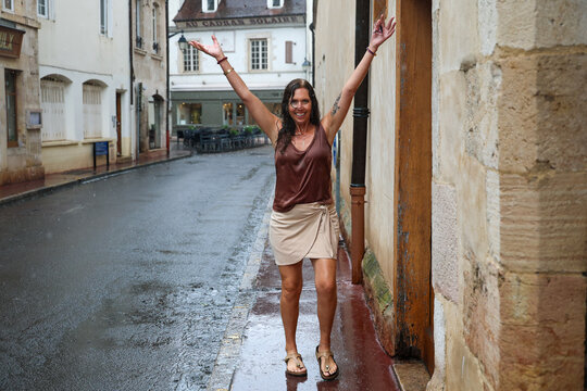 Woman walking along a rain-soaked street in Beaune, France, after a summer shower, surrounded by historic architecture in the heart of Burgundy.