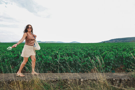 Woman walking beside vineyards in Puligny-Montrachet, Burgundy, France, surrounded by expansive wine country landscapes and historic viticultural heritage.