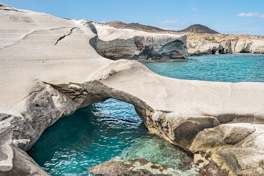Natural rock arch over turquoise coastal water in Milos island, Greece.
A rugged natural rock arch spans clear turquoise seawater along a beige coastal landscape in the Aegean sea.