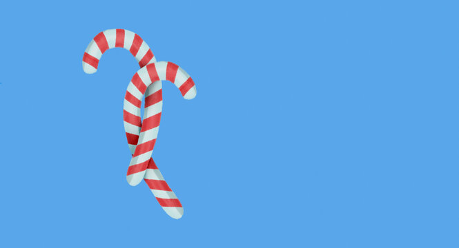 Two red and white striped peppermint candy canes crossed together on a solid bright blue background with copy space