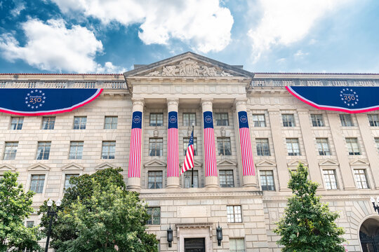 Freedom 250 bunting frames the Commerce building pediment beneath dramatic Washington clouds.
