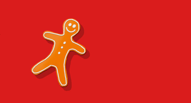 Smiling gingerbread man cookie decorated with white icing on a solid vibrant red background with copy space