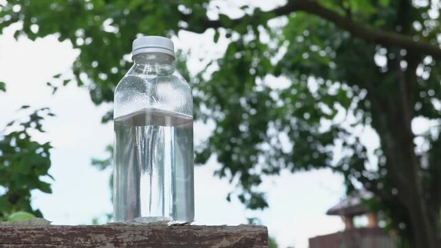 A transparent plastic water bottle on the surface with trees and a blue sky in the background and warm sunlight, a refreshing drink and natural hydration in the fresh air surrounded by pure nature