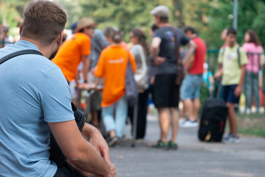man sitting with a blue suitcase near a crowd of volunteers, outdoor scene with people in orange shirts, significant empty space for text, concept of travel, humanitarian aid, refugee assistance
