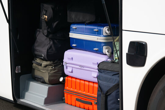  colorful suitcases and bags packed inside open luggage compartment of white bus, concept of tourism, travel agency, summer vacation