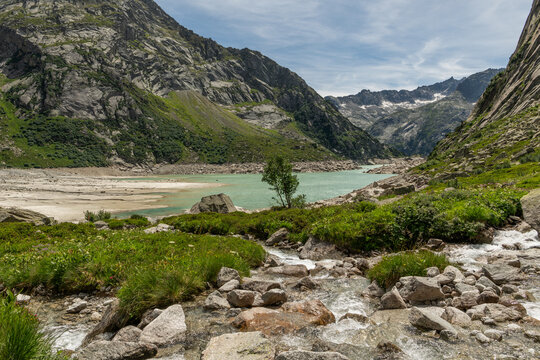 Guttannen, Switzerland. Mountain stream flowing into turquoise Gelmersee reservoir surrounded by alpine landscape in the Bernese Alps