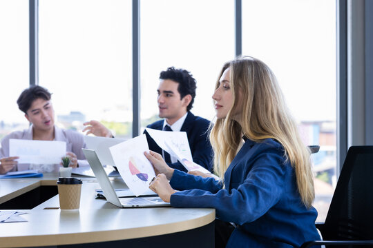 Focused businesswoman holding and reviewing a financial report document with colleagues during a corporate meeting in a modern office.
