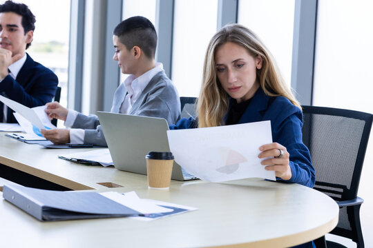 Focused businesswoman holding and reviewing a financial report document with colleagues during a corporate meeting in a modern office.