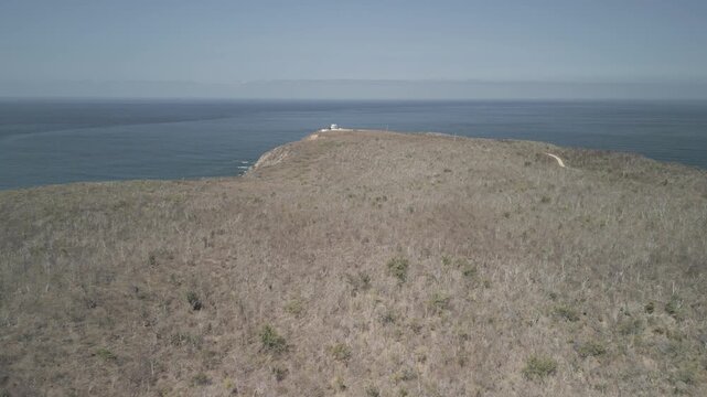 Aerial drone shot of a rocky coastline near Puerto Vallarta with a small building standing atop a cliff, shot in a flat log color profile for color grading, cinematic coastal landscape
