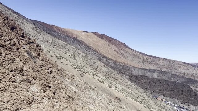 Breathtaking high angle view from moving cable car cabin ascending Teide volcano slopes in Tenerife. Beautiful panorama of desert mountain landscape, basalt layers and tiny tourist parking lot below.