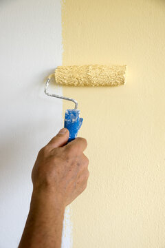 A man holds a paint roller and paints the wall with light yellow paint. Interior renovation work.