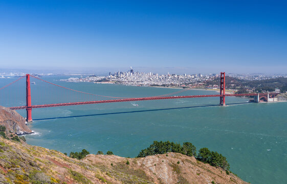 The Golden Gate Bridge spans the entrance of the bay with the San Francisco skyline visible from the rugged cliffs of the Marin Headlands.
