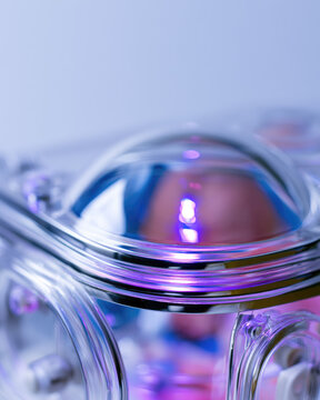 Premature baby incubator close up with soft purple light and reflective acrylic glass, clean medical care mood