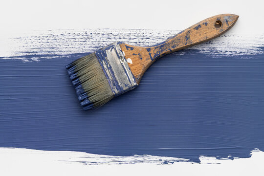 Vintage worn paintbrush on blue paint stroke over white background