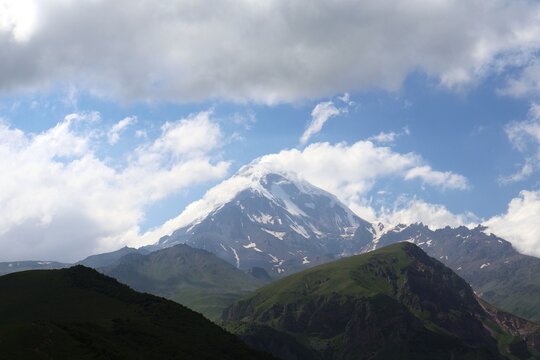 Snow covered summit of Mount Kazbegi emerging through clouds in Greater Caucasus range