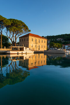 Scenic morning waterfront view of Jelsa town on Hvar island, Croatia. Traditional Mediterranean stone architecture, pine trees and boats reflecting in calm Adriatic sea during golden hour.