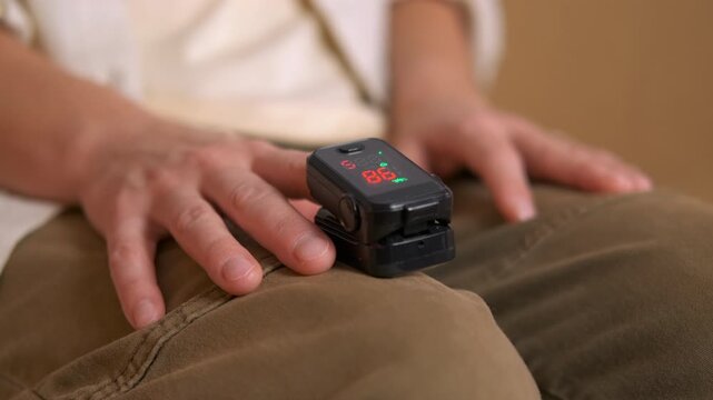 Person measuring oxygen saturation and pulse rate with fingertip oximeter. Close-up of a person's hands while using a portable pulse oximeter to check their blood oxygen saturation level