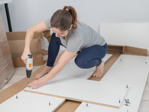 A Caucasian woman uses a screwdriver to tighten a screw while assembling a cabinet.