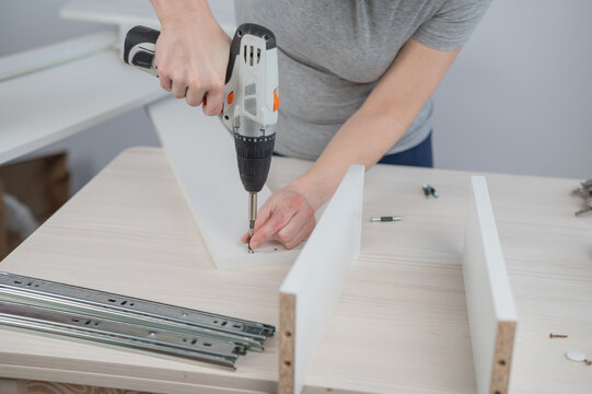 A Caucasian woman uses a screwdriver to tighten a screw while assembling a cabinet.