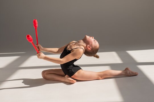 Little gymnast posing with clubs on white background. 