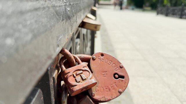 Rusty wedding locks hang securely on a metal bridge railing. A red heart padlock symbolizes romantic commitment and eternal love. This sweet scene brings a joyful and nostalgic feeling.