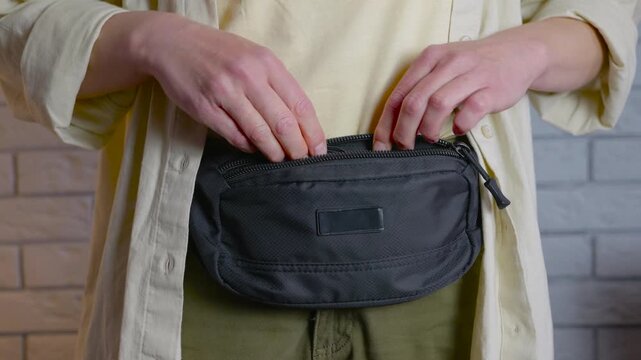 Woman hiding passport and money in a fanny pack for travel. Cautious woman securing her passport and a large sum of us dollar bills inside a belt bag, demonstrating a safe way to passport and cash