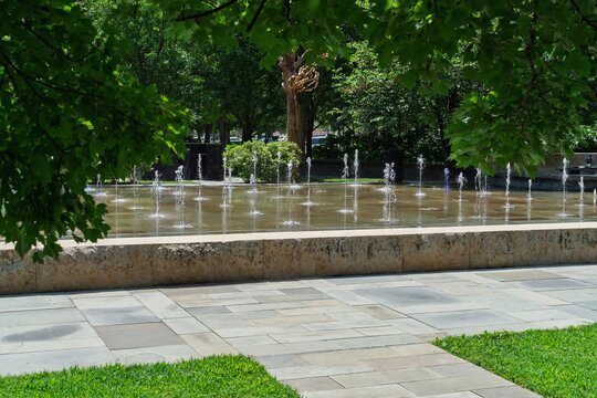 Splash fountain jets in park plaza framed by green trees