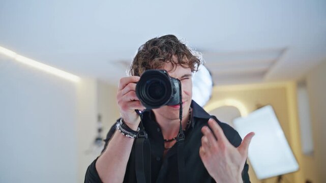 Cameraman aiming lens at viewer. Young man taking photos studio session.