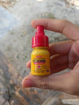 Bangka Belitung, INDONESIA - JULY 30, 2026: A person holding a small 10ml yellow bottle of Ecodine Povidone Iodine antiseptic solution by Onemed in their palm, used for first aid and wound care.