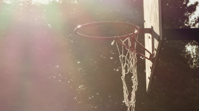 A basketball hoop glows under dreamy, warm sunlight. This vintage scene evokes deep feelings of peace, nostalgia, and quiet hope. Green trees stand softly in the hazy background.