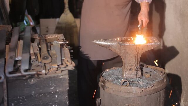 Close-up of a skilled blacksmith striking glowing hot metal with a hammer on an anvil, creating a shower of bright sparks. Traditional forging and metalworking.