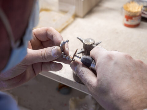 Dental technician finishing metal bridge framework with rotary handpiece, precision laboratory workflow for restorative dentistry, custom prosthesis and skilled healthcare craftsmanship.