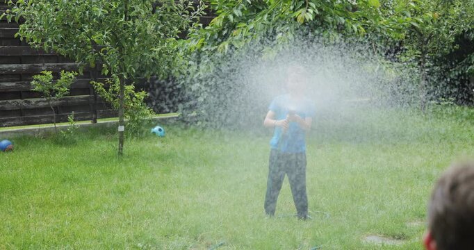 Little boy spraying water towards his brother in the garden