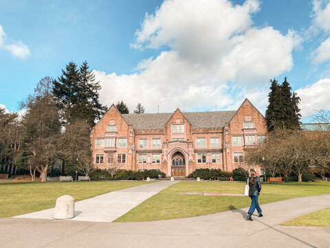 A woman walks along a path on the University of Washington campus in front of a historic brick building. - 12.04.2024, Seattle WA, USA