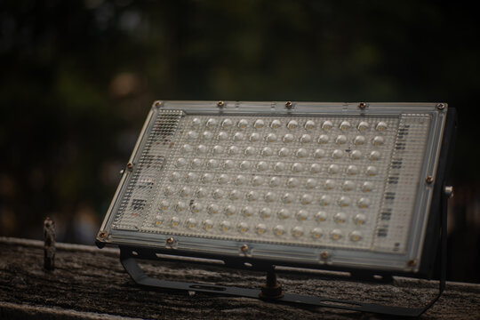 LED floodlight, outdoor lamp, glass cover, metal frame, weathered wood, dark forest background with industrial lighting fixture on rustic surface for energy efficient illumination